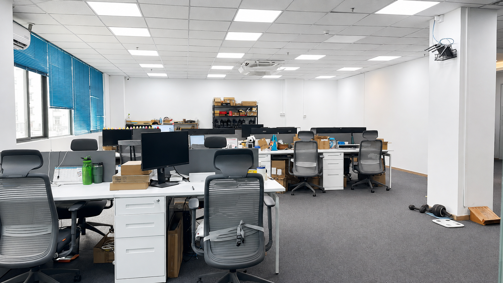 Hulin’s Shenzhen office with desks, monitors, engineering materials and blue window blinds.