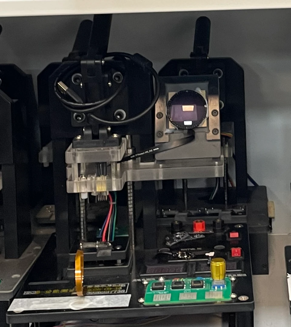 Supplied PCBA testing-equipment detail with contact pins, exposed boards, cables and a display.